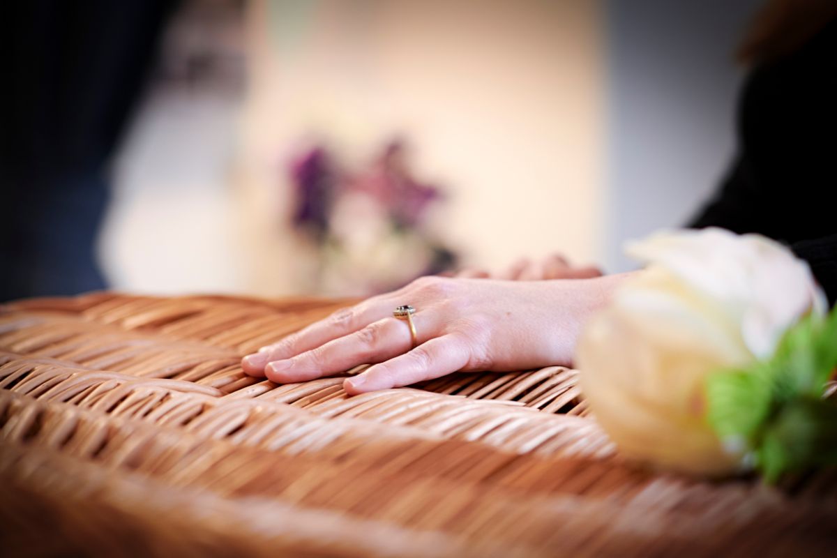 White rose on a wooden coffin with a family member's hand resting on the top.